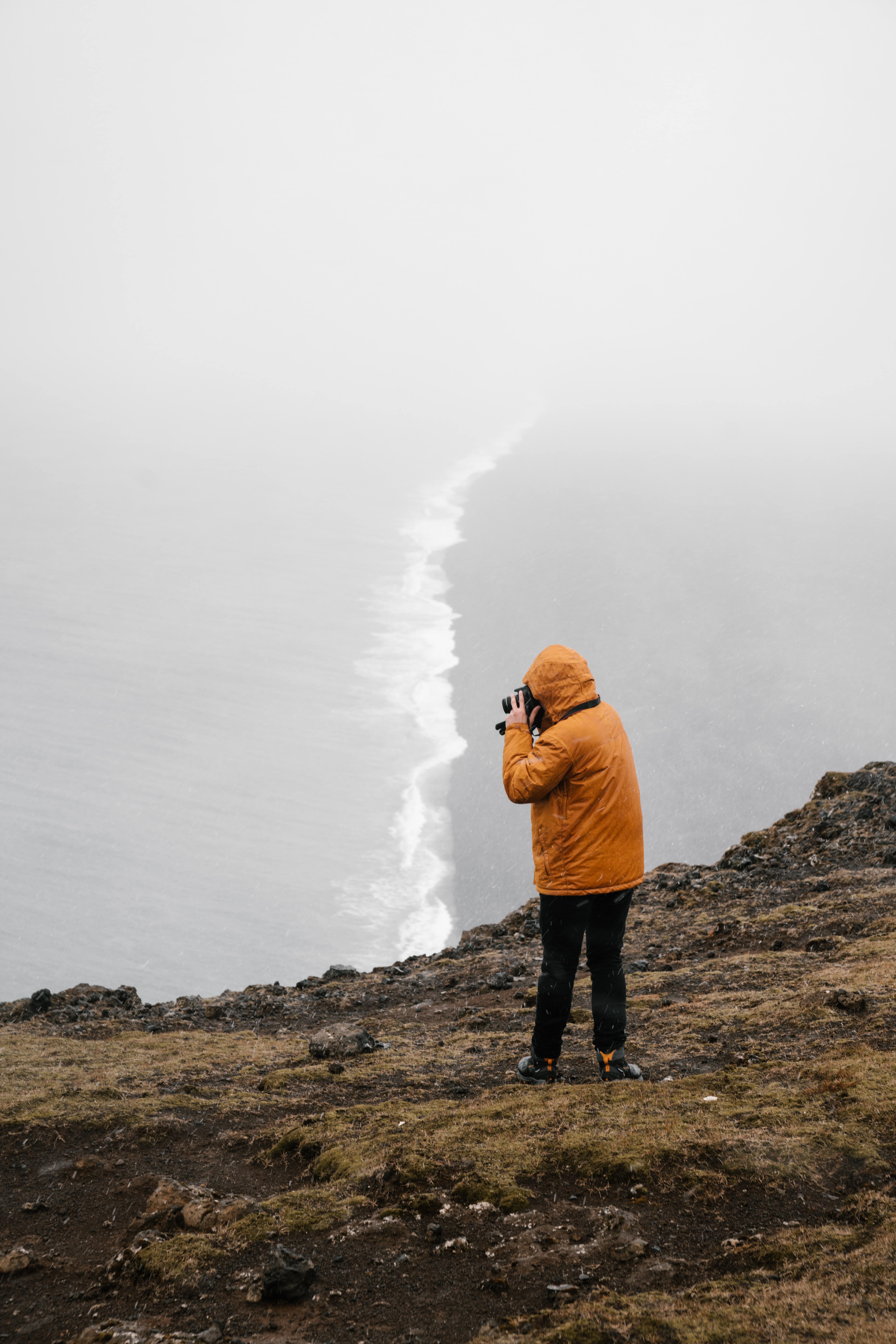 a person with a raincoat on taking a picture of the stormy sea